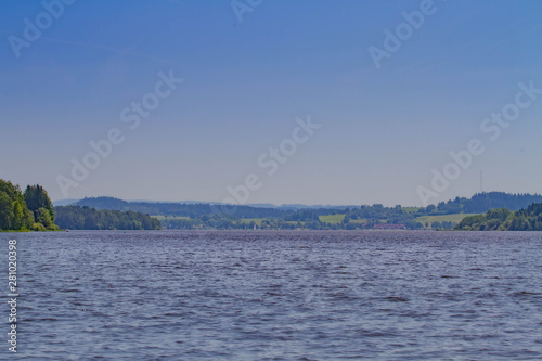 The Lipno Dam - Horni Plana, Czech Republic, in a bright summer day. The lake is calm, has clean blue water. There are no clouds in the sky. Lot of trees on the background.