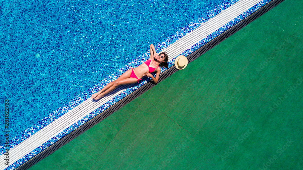 Attractive woman tourist in bikini sunbathes in scorching hot tropical summer. Sexy young woman sleeps on the edge of the crystal clear pool in her new bikini. Top view
