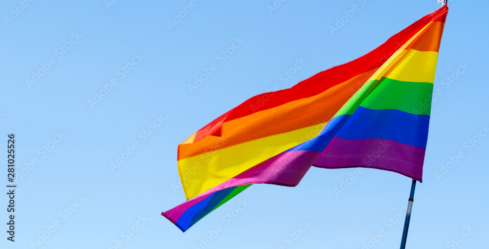 Obraz premium Gay rainbow flag waving in the wind in a clear blue sky