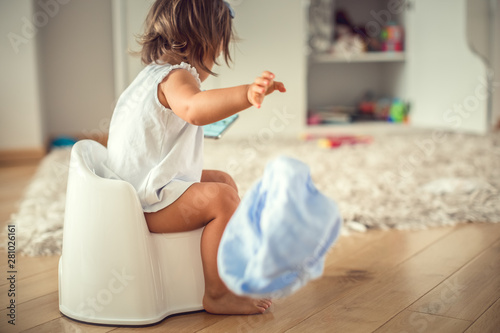 Tableau sur toile Toddler girl sitting on training toilet while using a smartphone
