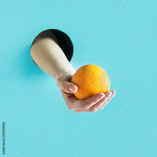 Fototapeta Naklejka Na Ścianę i Meble -  Female hand holding ripe orange in paper hole.