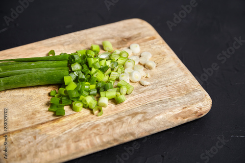 Scallion, fresh green onions sliced on a wooden cutting board on black background. Organic food ingredient