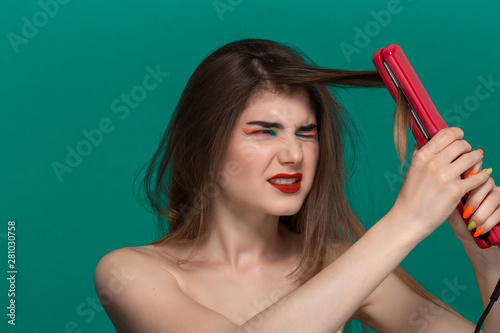 Portrait of beautiful young woman with bright color make-up having probems doing hair style herself with a purple straightening iron photo