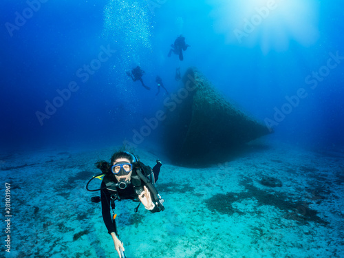 Scuba Taucherin vor einem gesunkenen Wrack gibt das OK Signal im tiefen, blauen Ozean © moofushi