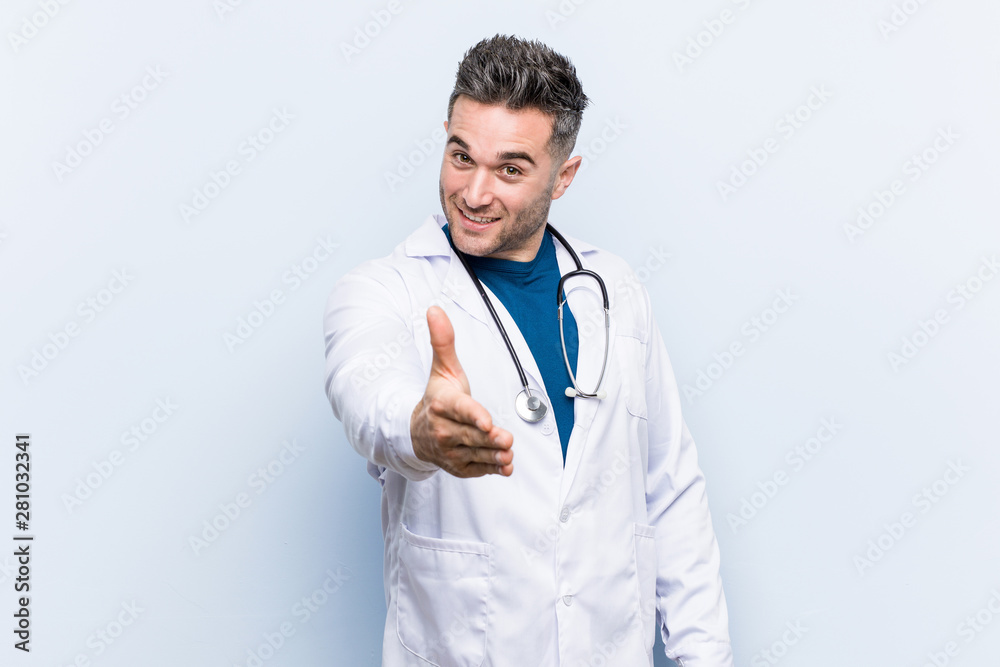 Young handsome doctor man stretching hand at camera in greeting gesture.