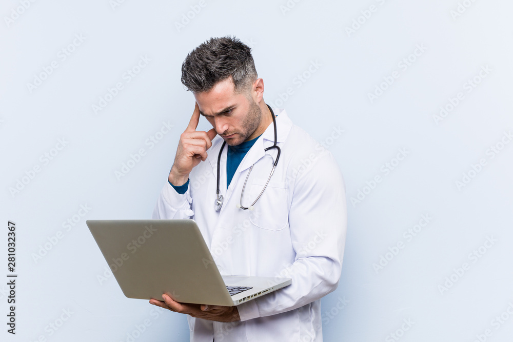 Caucasian doctor man holding a laptop pointing his temple with finger, thinking, focused on a task. Caucasian doctor man holding a laptop pointing his temple with finger, thinking, focused on a task.
