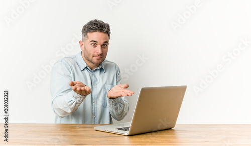 Young handsome man working with his laptop holding something with palms, offering to camera.