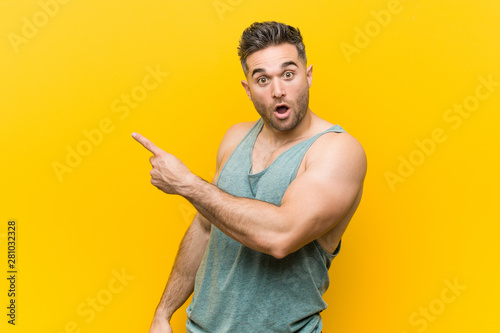 Obraz na plátně Young fitness man against a yellow background pointing to the side