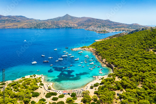Der beliebte Strand auf der kleinen Insel Moni gegenüber von Perdika bei Ägina mit türkisem Meer und zahlreichen Segelbooten, Griechenland