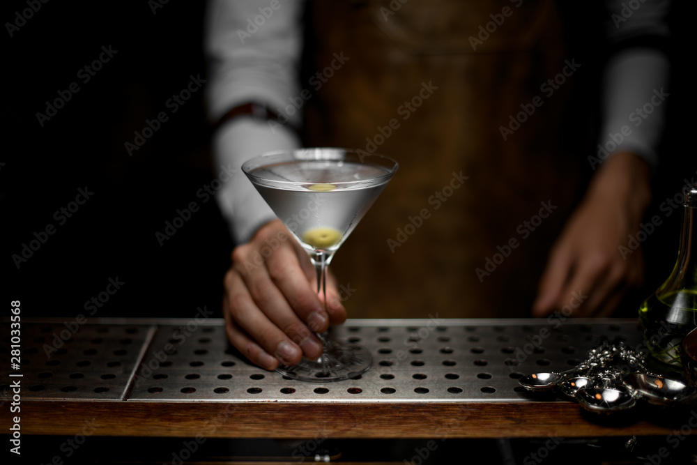 Bartender holds glass with martini on counter