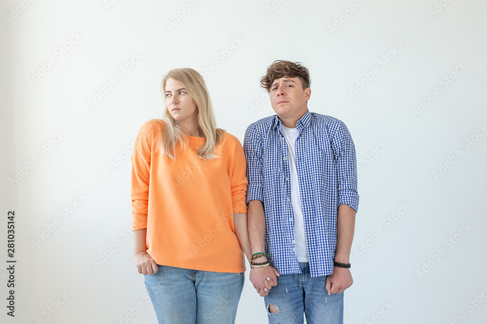 Young funny couple charming serious girl and a crazy young guy in casual clothes holding hands and posing on a white background. Misunderstandings in the relationship concept. Copyspace. Young funny couple charming serious girl and a crazy young guy in casual clothes holding hands and posing on a white background. Misunderstandings in the relationship concept. Copyspace.
