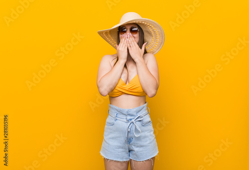 Young caucasian woman wearing a straw hat, summer look laughing about something, covering mouth with hands.