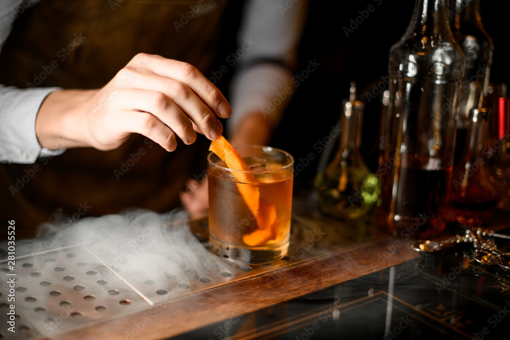 Bartender puts orange zest in whiskey glass
