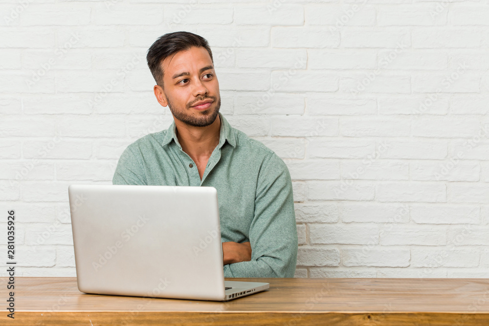 Young filipino man sitting working with his laptop smiling confident with crossed arms. Young filipino man sitting working with his laptop smiling confident with crossed arms.