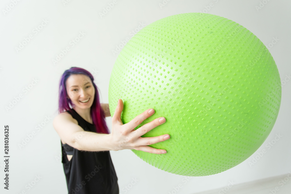 Fototapeta premium Blurred young positive cheerful girl hipster holding a green fitball in her arms during classes in the gym. Concept of yoga and pilates and fitness.