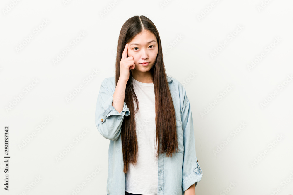 Young asian woman pointing his temple with finger, thinking, focused on a task. Young asian woman pointing his temple with finger, thinking, focused on a task.