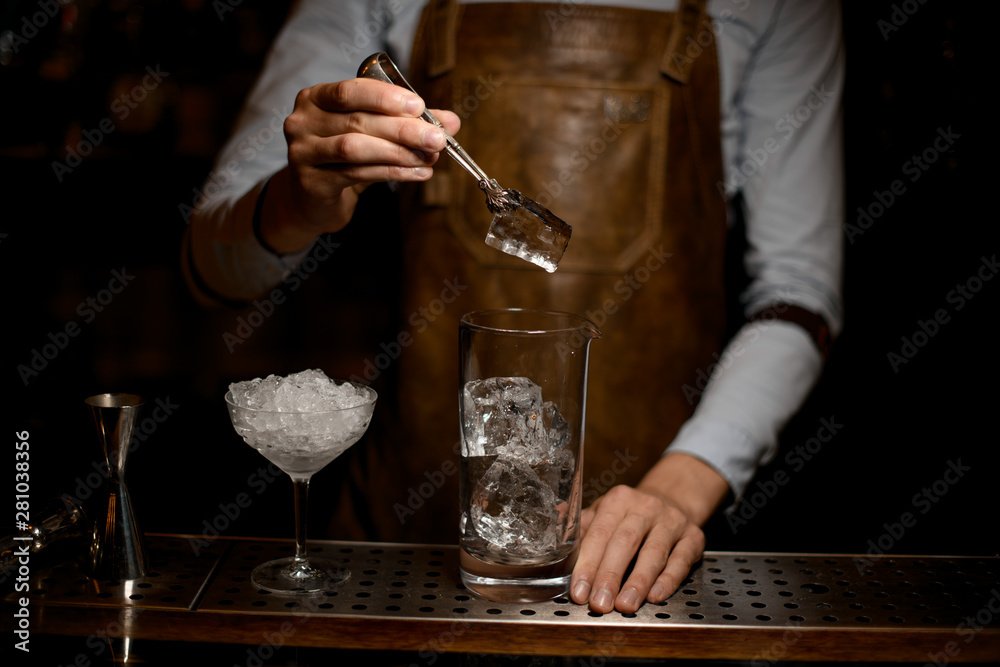 Bartender puts ice in cocktail glass with tongs