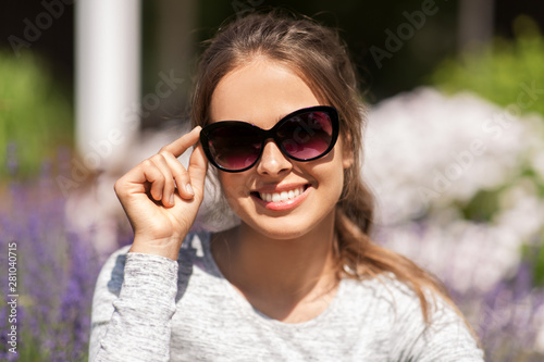 summertime, leisure and people concept - portrait of happy young woman in sunglasses at summer garden