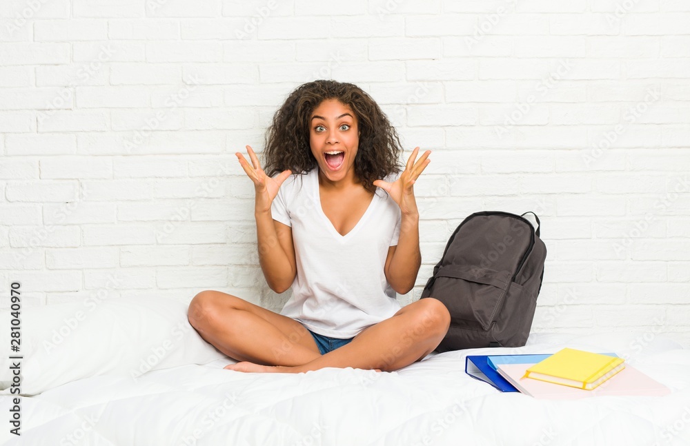 Young african american student woman on the bed celebrating a victory or success, he is surprised and shocked. Young african american student woman on the bed celebrating a victory or success, he is surprised and shocked.