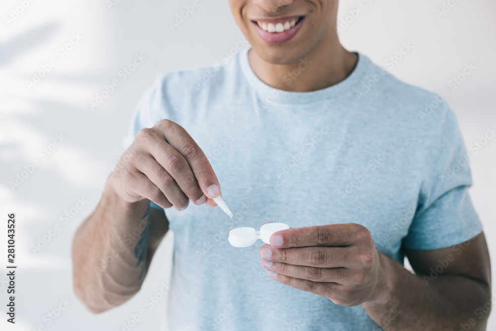 cropped view of man holding container and taking contact lens with tweezer cropped view of man holding container and taking contact lens with tweezer