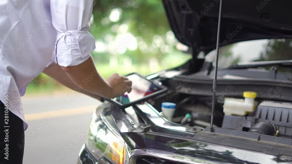 A young Asian man examines his broken car on the side of the road. A young Asian man examines his broken car on the side of the road.
