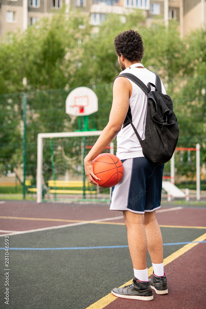 Young active male basketball player with ball and backpack on playground