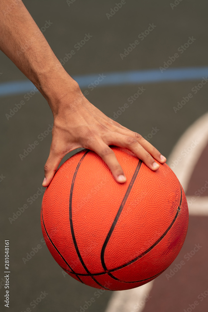 Hand of young active basketballer holding ball while getting ready to throw it