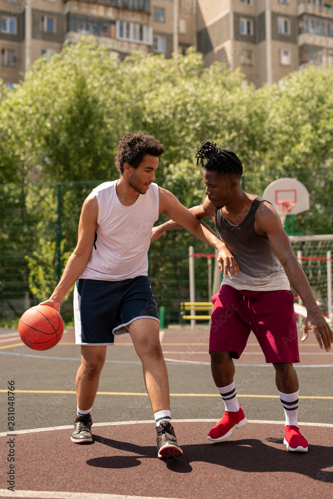 Two intercultural basketball playmates playing or training on the court