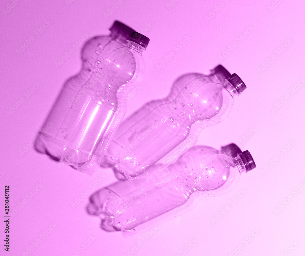 Transparent plastic bottle on a purple background. Hard shadows on the background.