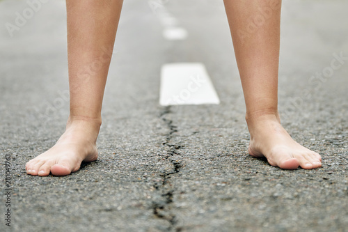 Bare feet of a young girl stand on the asphalt road close up. © Georgy Dzyura