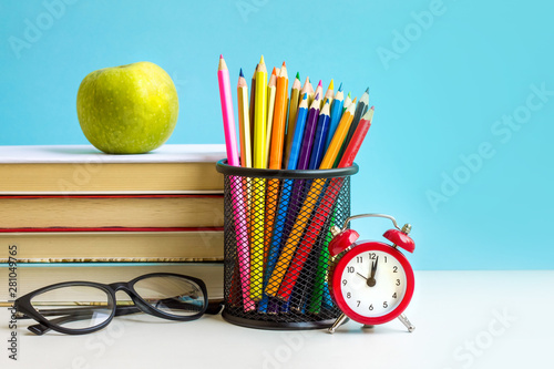 Back to school concept. Red alarm clock, apple, color pencils, books on a blue background. September 1st concept.