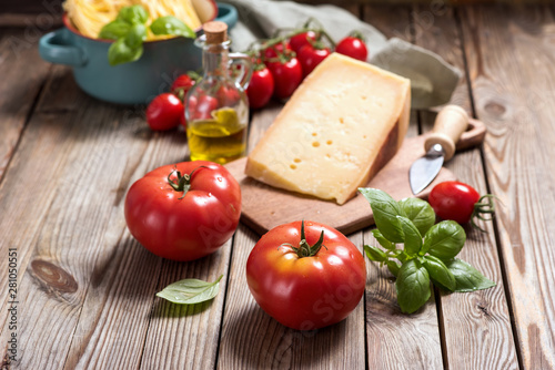 Cooking ingredients for italian cuisine, unsooked pasta, parmesan cheese, tomatoes, herbs on wooden background