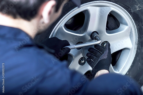 Back view mechanic in blue jumpsuit is repairing car at service station. Closeup repairman hands are unscrewing nuts on disk with wrench to remove wheel at auto repair shop.Tire fitting concept.