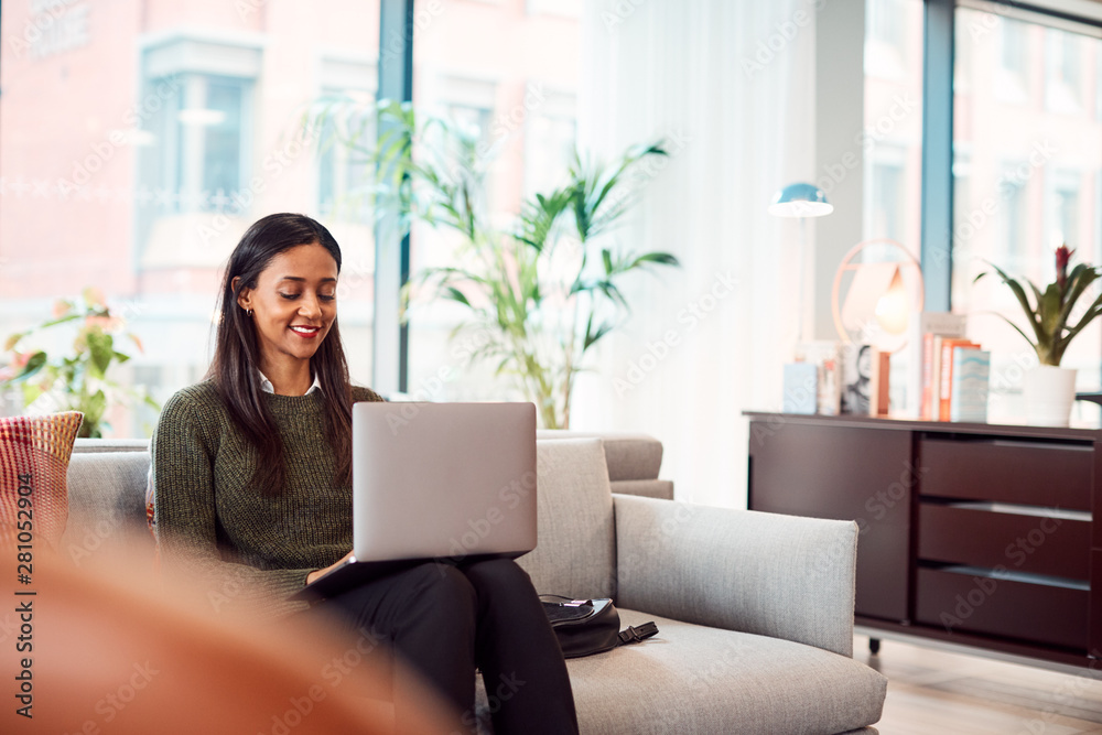 Naklejka premium Businesswoman Sitting On Sofa Working On Laptop At Desk In Shared Workspace Office