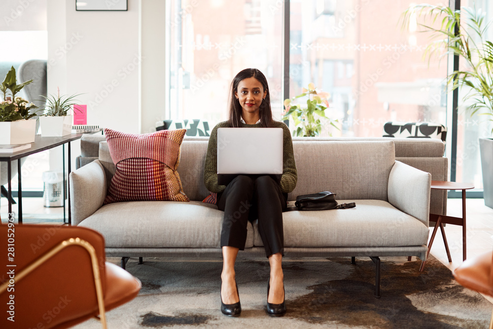 Portrait Of Businesswoman Sitting On Sofa Working On Laptop At Desk In Shared Workspace Office Portrait Of Businesswoman Sitting On Sofa Working On Laptop At Desk In Shared Workspace Office