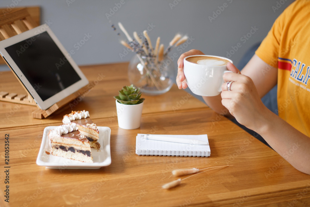 coffee in a Cup in the hands of a girl in a yellow t-shirt on a wooden table with a notebook and a tablet in the cafe work in the morning coffee in a Cup in the hands of a girl in a yellow t-shirt on a wooden table with a notebook and a tablet in the cafe work in the morning
