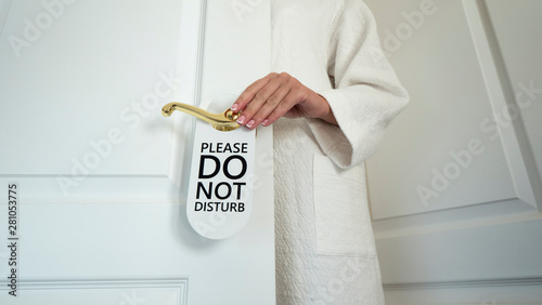 Unrecognizable woman in a white house coat hangs a sign on the door Do not disturb