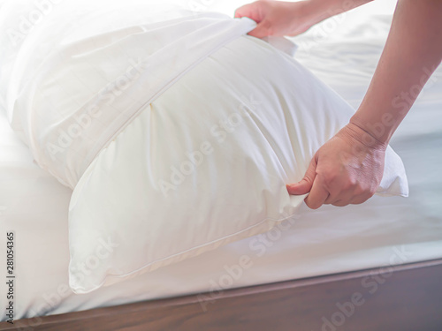 White pillow on the bed in the bedroom with woman 's hand who are making the room.