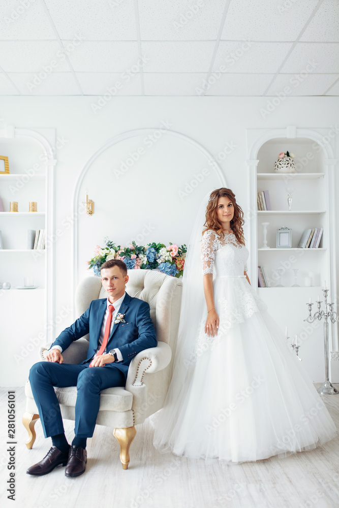 Beautiful bride in white dress and groom in suit, posing in white Studio interior, wedding Beautiful bride in white dress and groom in suit, posing in white Studio interior, wedding