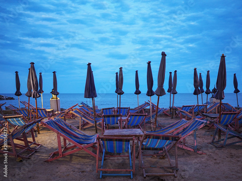 Many wooden deckchairs and umbrellas on sand at sunset beach.