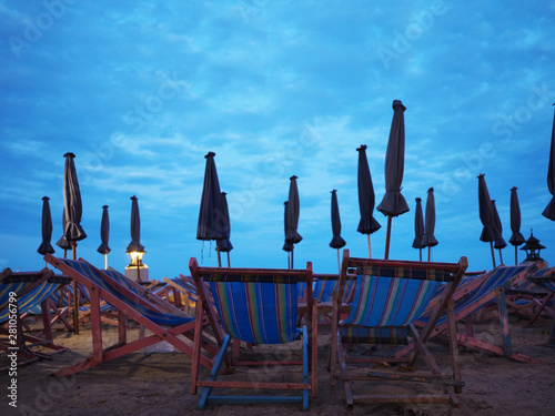 Many wooden deckchairs and umbrellas on sand at sunset beach.