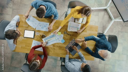 Startup Meeting Room: Team of Entrepreneurs sitting at the Conference Table Have Discussions, Solve Problems, Use Digital Tablet, Laptop, Share Documents with Statistics, Charts
