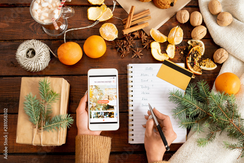 Female hands holding smartphone and making list of Christmas gifts photo