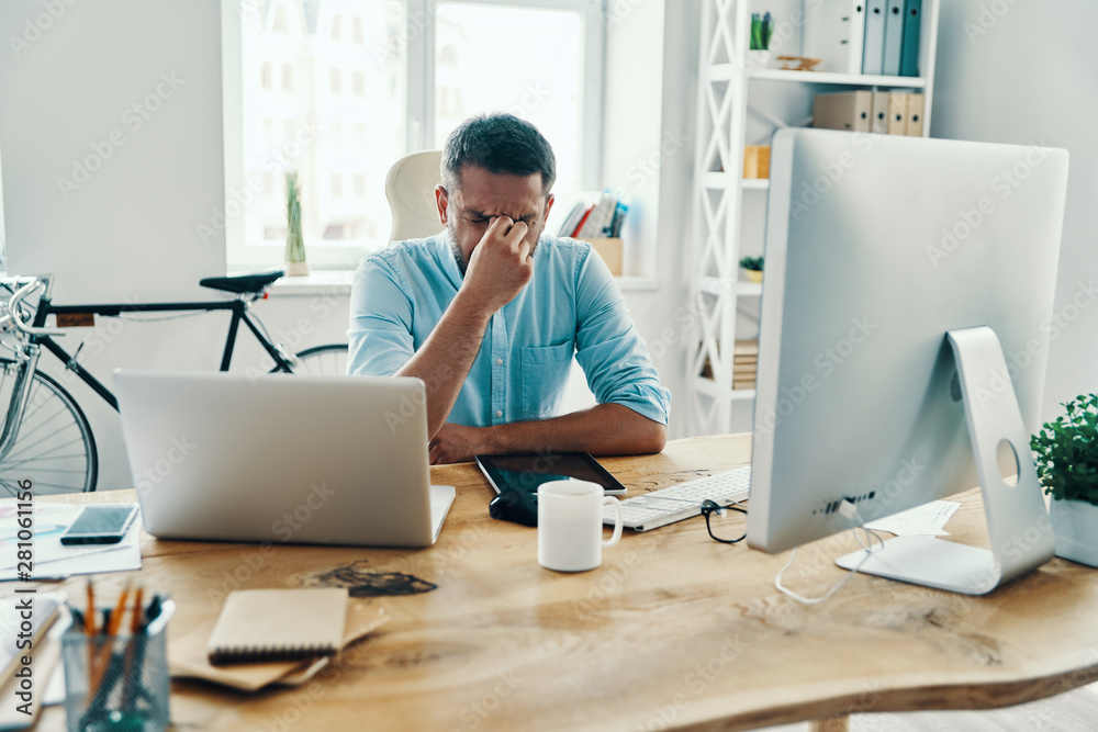 Frustrated middle age man in smart casual wear massaging nose while sitting in the office Frustrated middle age man in smart casual wear massaging nose while sitting in the office