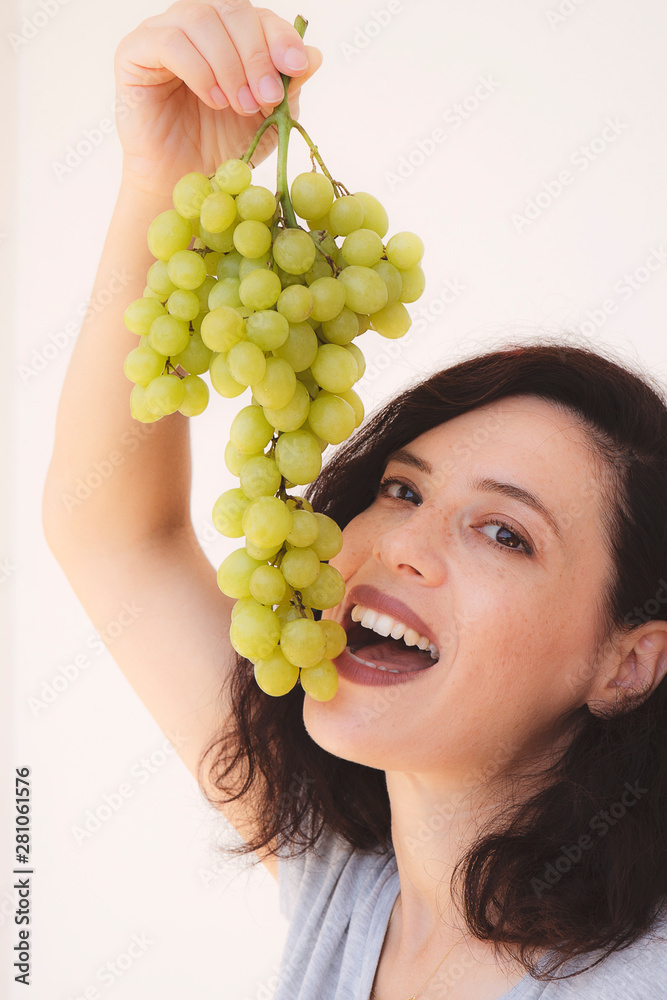 Smiling girl holding grapes near her face and smiling broadly to the viewer. Concept of home brew vine. Vertical image Smiling girl holding grapes near her face and smiling broadly to the viewer. Concept of home brew vine. Vertical image