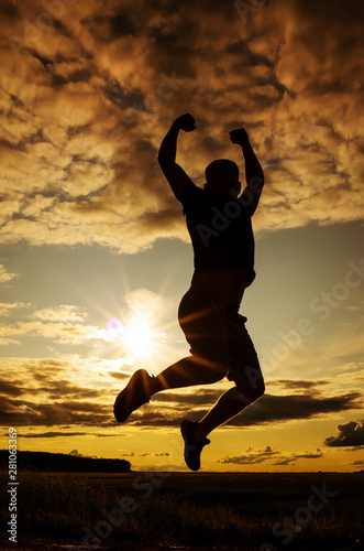 Silhouette of a young man in a jump against the backdrop of the setting sun and sky. The concept of happiness, activity, freedom, health. Man of dense build in a t-shirt and shorts. Place for text. © Ольга Холявина