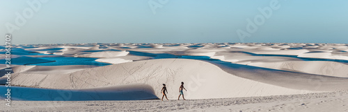 travel couple trek across giant sand dunes with lagoons in Lencois Maranhenses, one of the most stunning tourist attractions in North-East Brazil