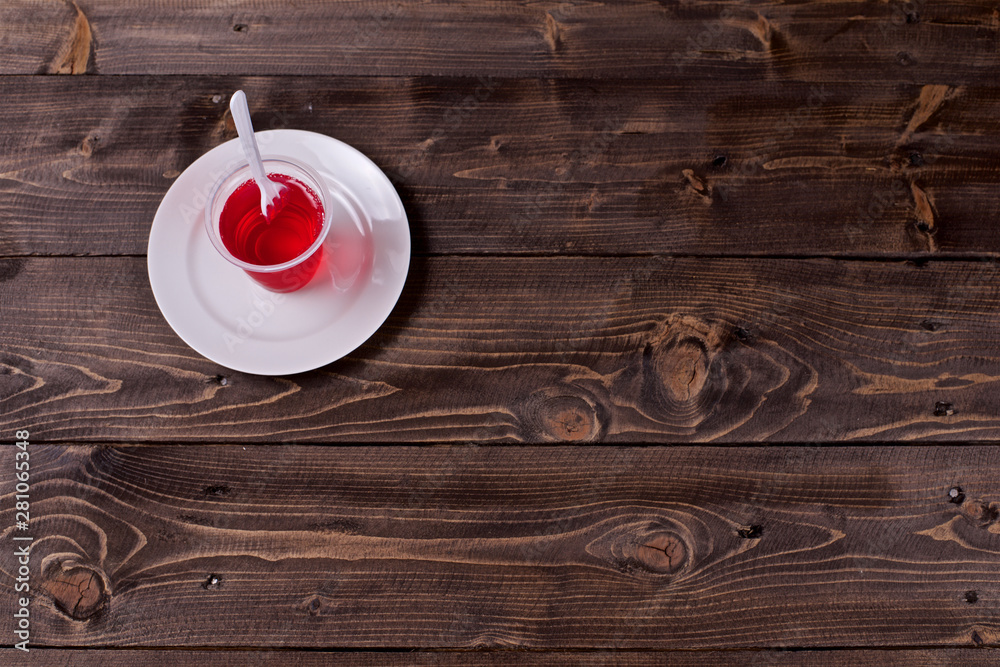 Berry jelly in a plastic Cup with a fork in a white plate on a wooden background Berry jelly in a plastic Cup with a fork in a white plate on a wooden background