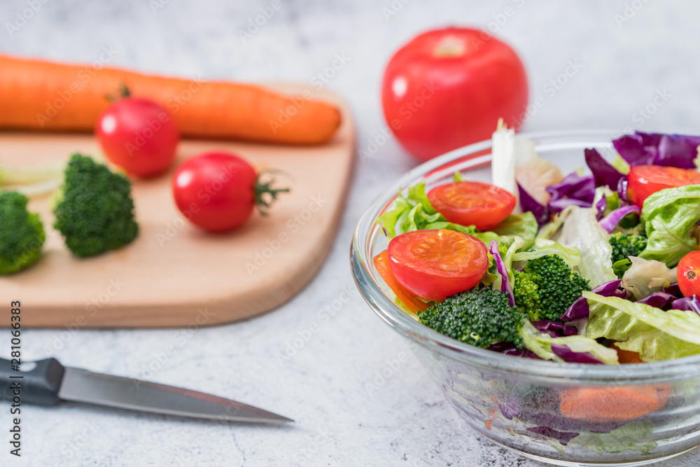 A bowl of vegetable salad and various vegetables on a cutting board A bowl of vegetable salad and various vegetables on a cutting board