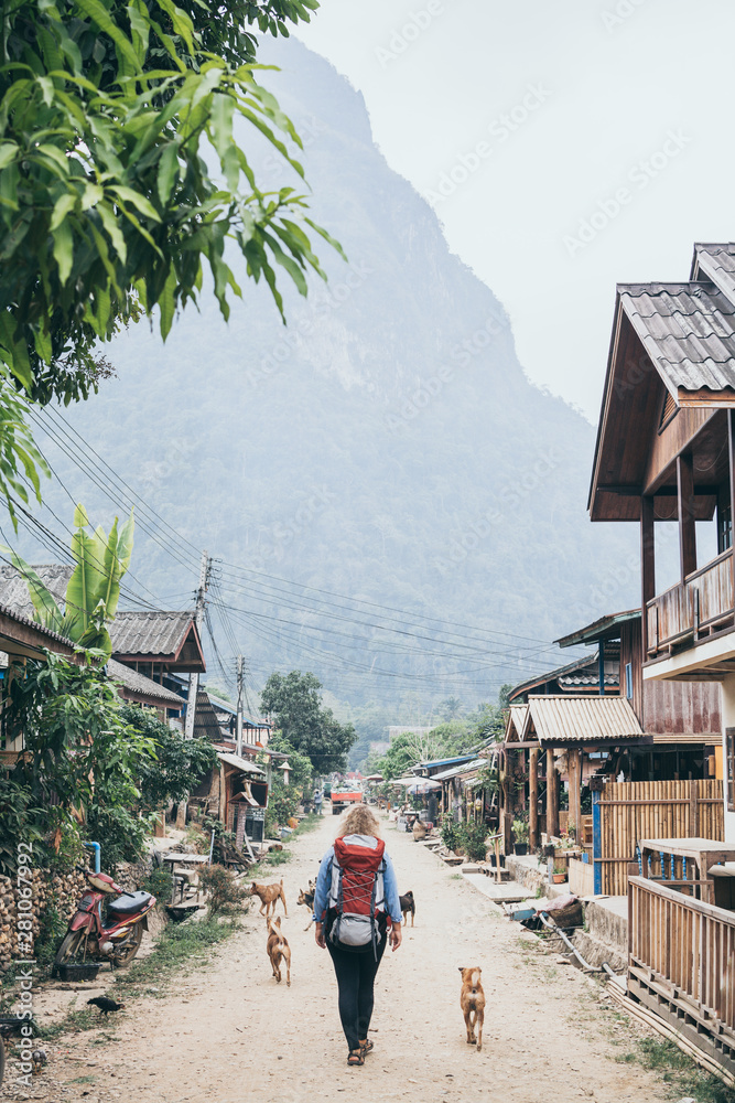 Young Caucasian blonde woman with backpack walking on the central street of Muang Ngoi village, Laos Young Caucasian blonde woman with backpack walking on the central street of Muang Ngoi village, Laos